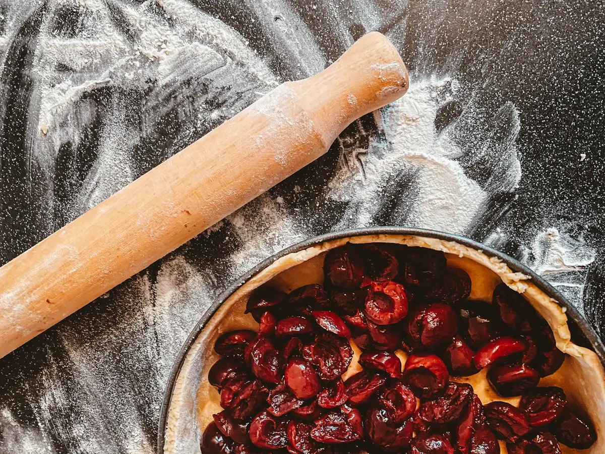 A rolling pin beside a bowl of cherries on a floured table